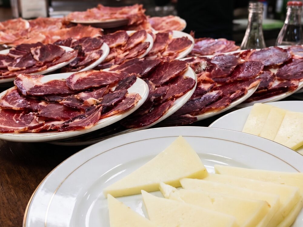 Pratos de presunto fatiado alinhados no balcão e um prato de queijo às fatias em primeiro plano