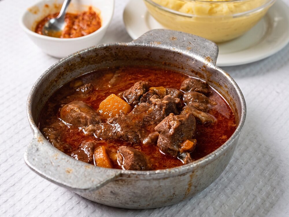 Caçarola de metal com vitela estufada em molho, com cenoura, e um puré de batata ao lado